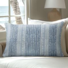 a blue and white pillow sitting on top of a couch next to a window with the ocean in the background