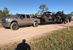 a large truck hauling an army vehicle down a road in front of a person standing on the side of the road