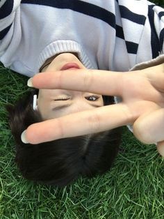 a woman making the v sign with her hand on top of her head while laying in the grass