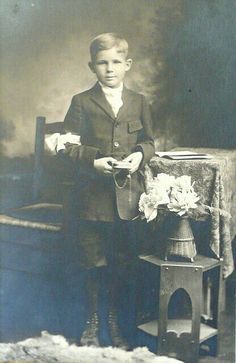 an old black and white photo of a young boy standing next to a table with flowers on it