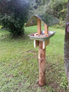 a bird feeder in the shape of a house on top of a wooden pole next to a tree