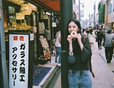 a woman standing on the side of a street holding a donut in front of her mouth