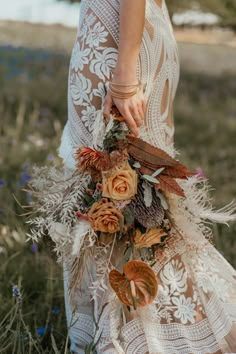 a woman in a white dress holding a bouquet with feathers and flowers on the grass