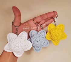 three small crocheted stars are being held by a person's hand with two key chains