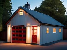 a white garage with red doors and lights on the windows at night in front of some trees