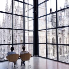 two people are sitting in chairs looking out the window at cathedrals and other buildings