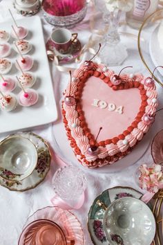 a heart shaped cake sitting on top of a table next to other plates and cups