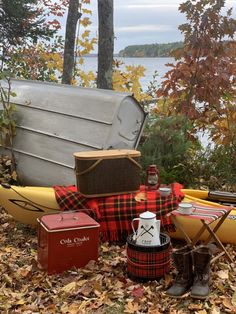 an assortment of camping gear sitting on the ground next to trees and water in fall