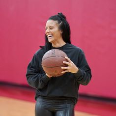 a woman holding a basketball in her right hand and laughing while standing on a court