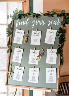 a seating chart is displayed on a easel with clothes pins and greenery around it