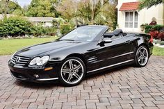 a black mercedes slk convertible parked in front of a house on a brick driveway