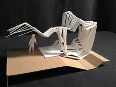 a sculpture made out of white paper on top of a cardboard box with a man standing in front of it