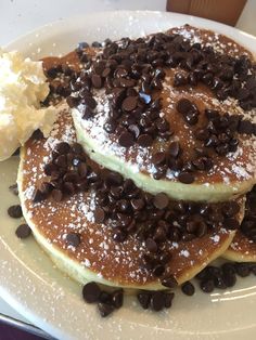 three pancakes with chocolate chips and butter on a white plate next to some ice cream