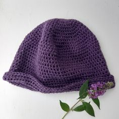 a purple crocheted hat sitting on top of a table next to a flower