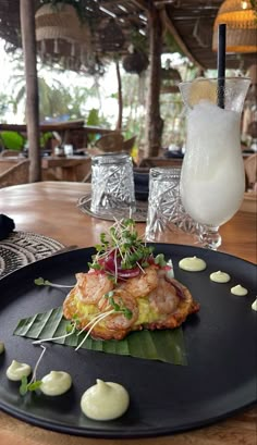 a black plate topped with food on top of a wooden table next to a drink