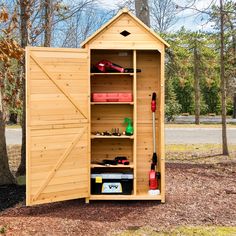 a storage shed with its doors open and tools in the door, next to a tree