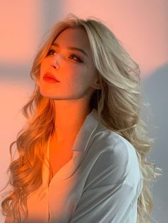 a woman with long blonde hair wearing a white shirt and looking off into the distance