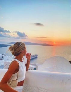 a woman standing on top of a white building next to the ocean at sun set