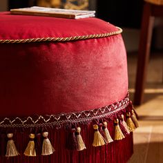 a red velvet ottoman with tassels and gold chains on the bottom is shown