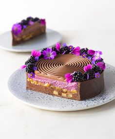 a piece of cake on a plate with purple flowers and blackberries around the edge