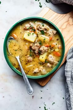 a bowl of soup with meat, potatoes and carrots on a wooden cutting board