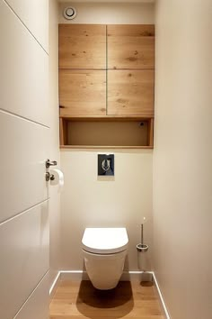 a white toilet sitting inside of a bathroom next to a wooden cabinet above the toilet