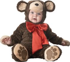 a baby in a bear costume sitting on the floor with its paws up to his chest