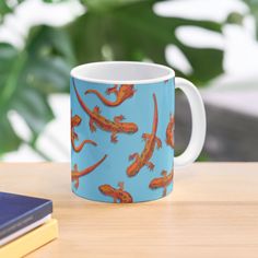 a blue mug with orange lizards on it sitting on a table next to a book