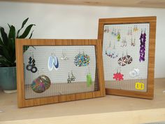 two wooden frames with earrings hanging from them on a shelf next to a potted plant