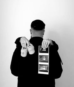 a man is holding two stuffed animals in his hands while standing against a white wall