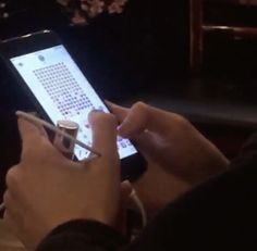 a person holding a cell phone in their right hand and writing on the screen with a pen