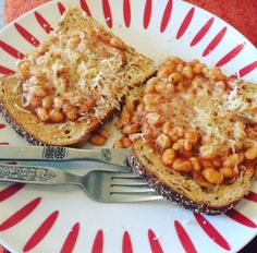 two pieces of toast topped with beans and cheese on a plate next to a fork