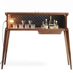 a wooden shelf with bottles and glasses on it, next to a light that is turned on