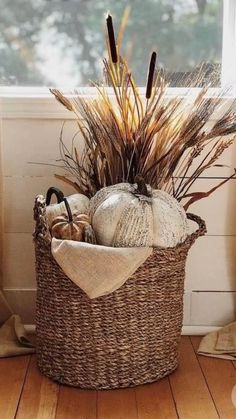 a wicker basket filled with pumpkins and other fall decorations in front of a window