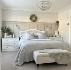 a bedroom with a white bed, dressers and a chandelier