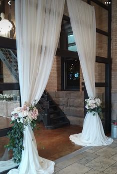 an outdoor wedding ceremony with white drapes and flowers on the aisle, set up in front of a brick building