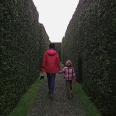 a woman and child walking down a path lined with hedges