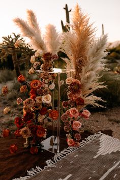 an arrangement of flowers and feathers in a vase on a table with a desert background