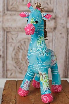 a blue and pink giraffe sitting on top of a wooden table next to a wall