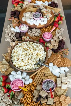 an assortment of snacks are arranged on a long table with bowls and spoons filled with marshmallows