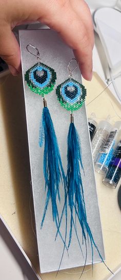 a pair of blue and green beaded earrings being held by someone's hand