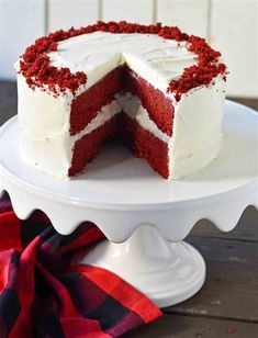 a red velvet layer cake with white frosting on a cake platter next to a plaid napkin