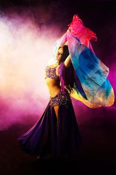 a belly dancer in purple and blue is posing with her colorful shawl over her head