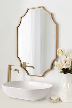 a white sink sitting under a mirror next to a vase with flowers