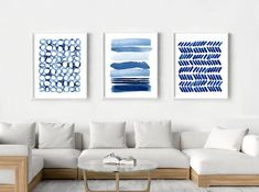 three blue and white paintings hang on the wall above a couch in a living room