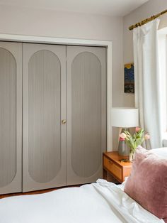 a bedroom with white bedding and two gray closets next to a lamp on a nightstand