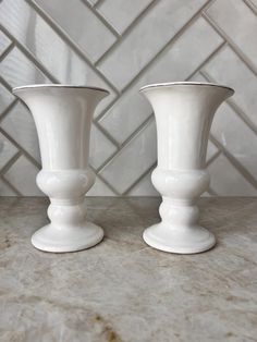 Add a touch of refined elegance to your home or event with this White Pedestal Urn Glass Vase. Its clean, classic design combines the beauty of a traditional urn with the delicacy of glass, creating a stunning centerpiece for any occasion. Whether you're looking for a sophisticated vase to showcase fresh flowers, or a unique decorative accent for your mantel, this timeless piece is sure to complement any space with its graceful and versatile appeal. Key Features: Material: Made of high-quality glass with a smooth, glossy finish that gives the piece a polished, timeless look. The white color ensures it pairs beautifully with any floral arrangement or decor style. Design: The vase features a classic pedestal urn shape with a gently flared bowl and an elegant base, offering both visual balanc Large White Vase, White Pedestal, Arrangement Floral, Vintage Inspired Decor, Entryway Console, Classic Home Decor, White Vase, Unique Display, Vase Vintage