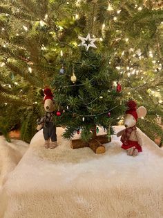 two small teddy bears sitting next to a christmas tree with lights on the treestop