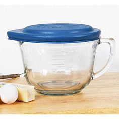 an empty glass measuring cup with blue lid next to eggs and cheese