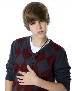 a young boy wearing a sweater and holding his hand on his chest while standing in front of a white background